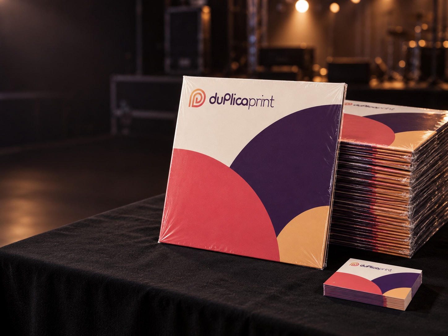 Pile de vinyles sous cellophane sur une table de merchandising, devant une scène de concert